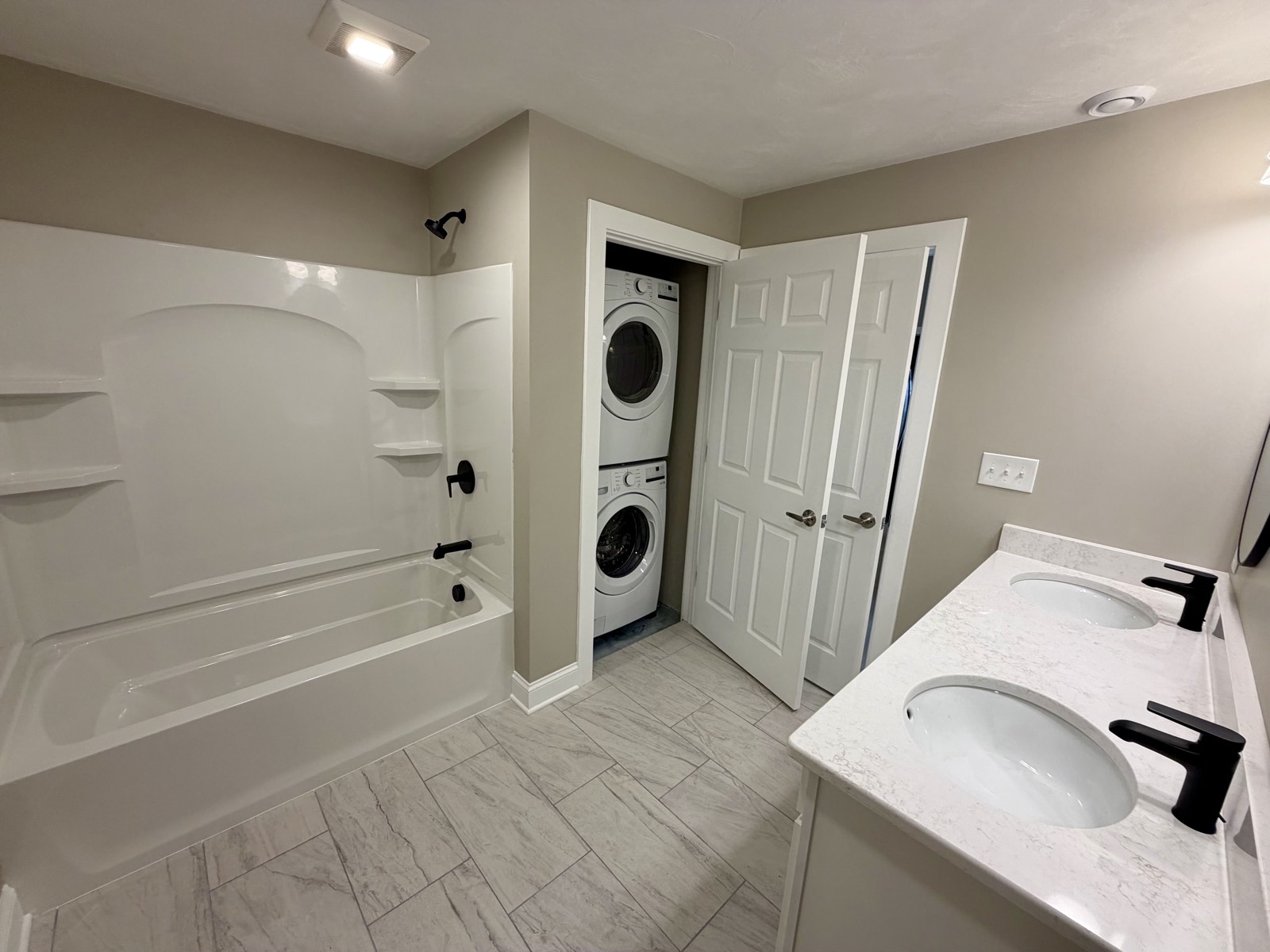 Bathroom with a full tub and shower beside a stacked washer and dryer.