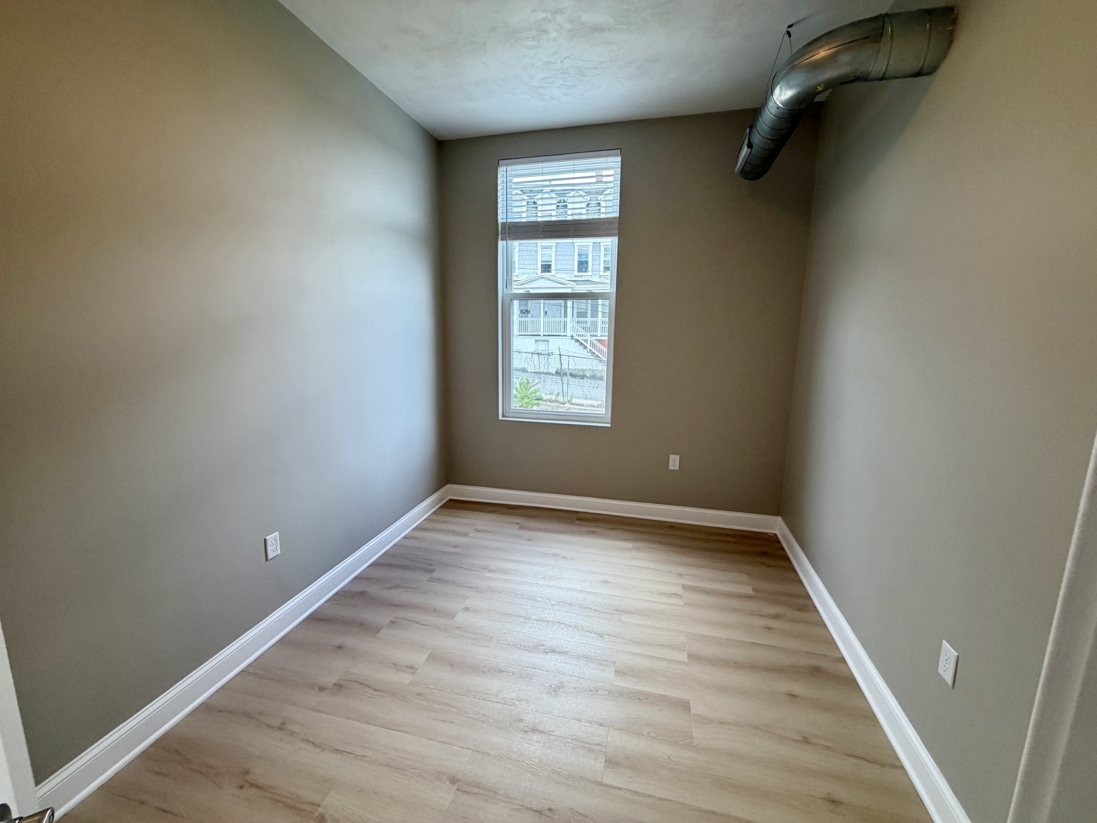 Bedroom corner with a window and wide-plank flooring.